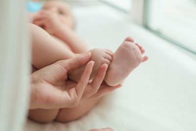 From above of adorable crop little feet of cute baby lying on bed on blurred background