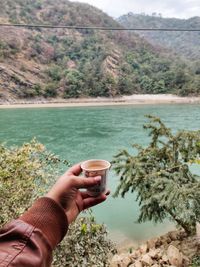 Beautiful photo of a male hand holding a cup of tea nearby a river in winter season.