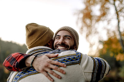 Young man embracing happy male friend wearing knit hat