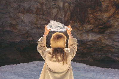 Rear view of woman standing on rock holding an ice piece