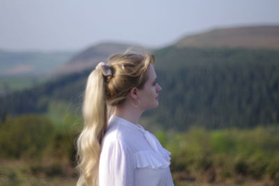 Side view of young woman standing on landscape