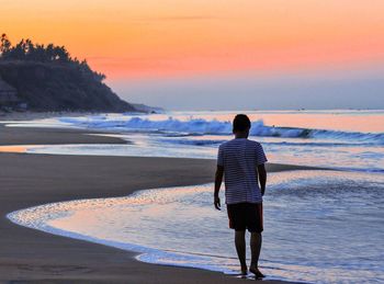 Rear view of man standing on beach during sunset