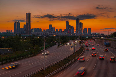 Cars on street by buildings against sky during sunset