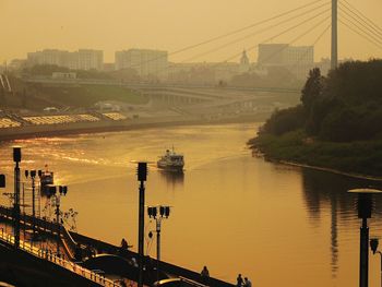 Ferry sailing in river at city against clear sky during sunset