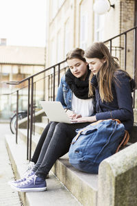 Young female friends using laptop on steps outside school