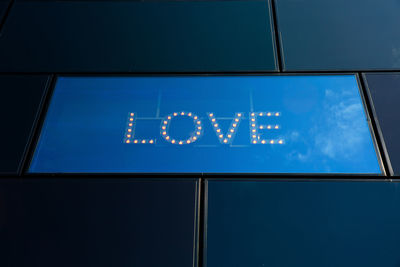 Low angle view of illuminated text on blue sign