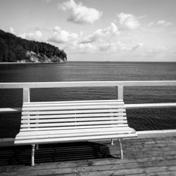 Bench on shore by sea against sky