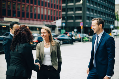 Smiling businesswomen greeting while male colleagues standing on sidewalk in city