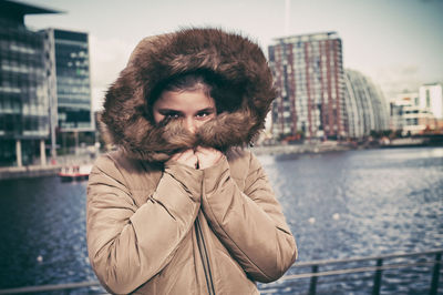 Portrait of young woman in warm clothing standing at riverbank