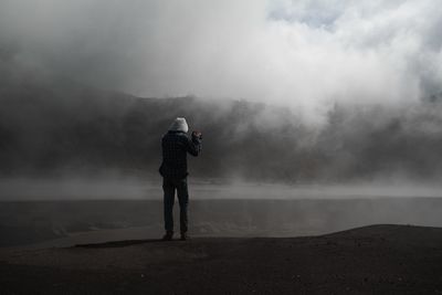 Rear view of man standing on rock against sky