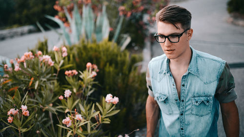 Young man wearing eyeglasses by flowers at park