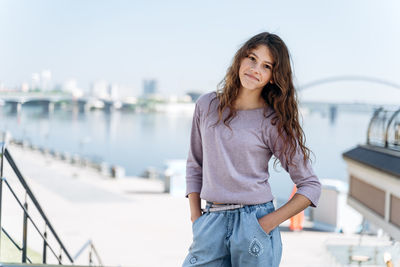 Portrait of smiling young woman standing against bridge