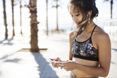 Sporty woman listening music through smart phone on footpath during summer