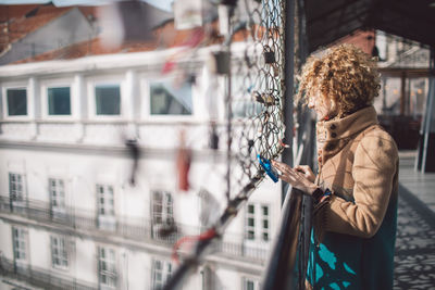 Woman looking through chainlink fence in city