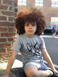 Portrait of cute boy with curly hair sitting outdoors