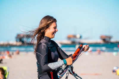 Portrait of young woman holding camera against sky