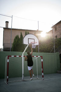 Rear view of mid adult man playing basketball against clear sky at sunset