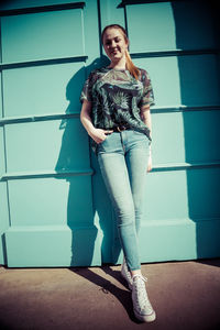 Portrait of smiling young woman standing against wall