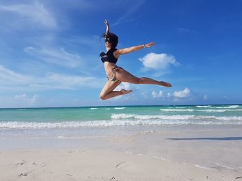 Low angle view of women jumping at beach against sky