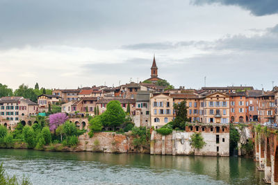 Buildings by river against sky in town