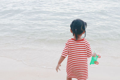 Rear view of girl holding toy standing at beach
