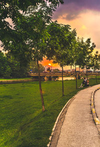 Footpath in park against sky during sunset
