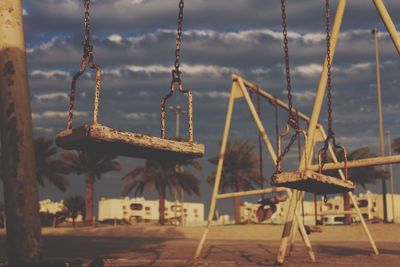 Empty swings in playground against cloudy sky