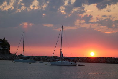 Sailboats in sea against sunset sky