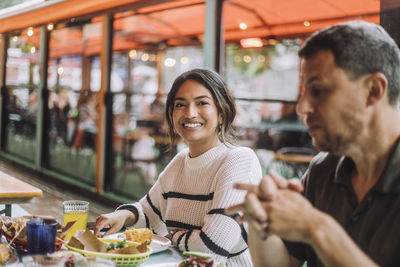 Portrait of smiling woman sitting with man while having food at restaurant