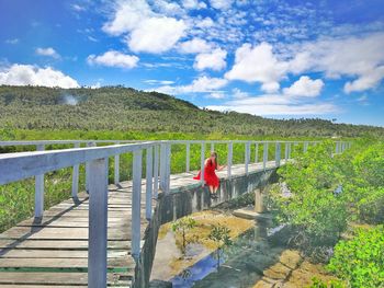 Woman sitting on bridge over landscape against sky