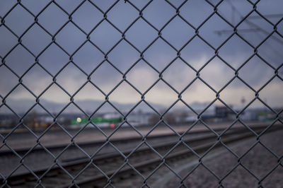 Railroad track seen through chainlink fence against cloudy sky