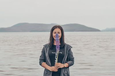 Portrait of woman holding flowers while standing against sea