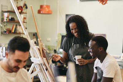 Cheerful female tutor with young student in front of painting in art class