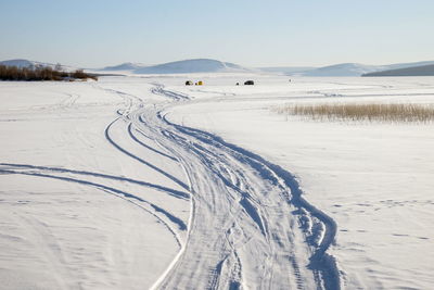 Trace from cars on a snowy lake with fishermen in the background