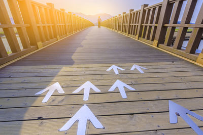 Low angle view of arrow sign on wooden bridge at sunset