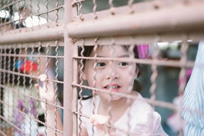 Girl looking away through metal fence