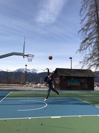 Man playing with basketball hoop against sky