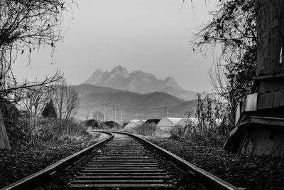 Railroad tracks leading towards mountains against clear sky