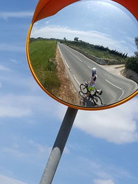 Woman riding bicycle on street seen in road mirror