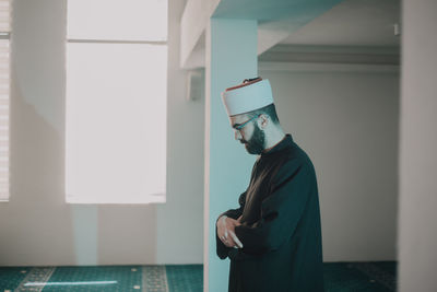 Side view of young man standing against window