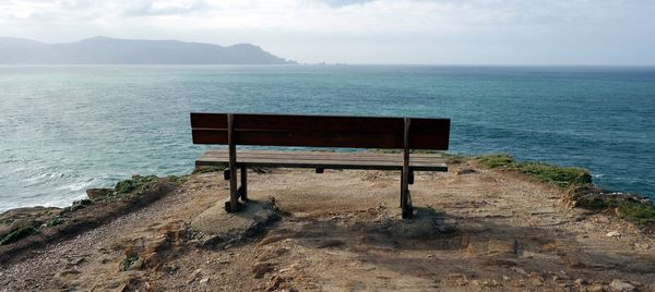 Empty bench on shore by sea against sky