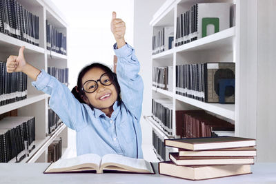 Portrait of smiling girl with arms raised while sitting in library