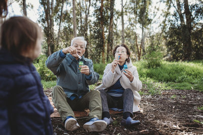 Grandmother and grandfather blowing bubbles for granddaughter outside