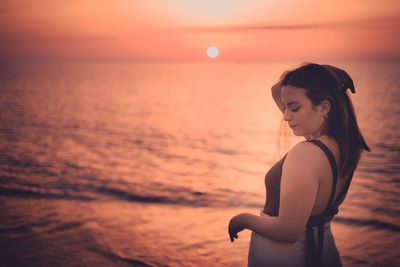 Woman standing by sea against sky during sunset