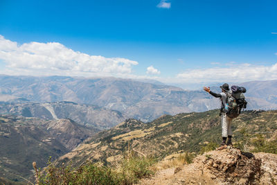 Rear view of man with arms outstretched standing on mountain against blue sky