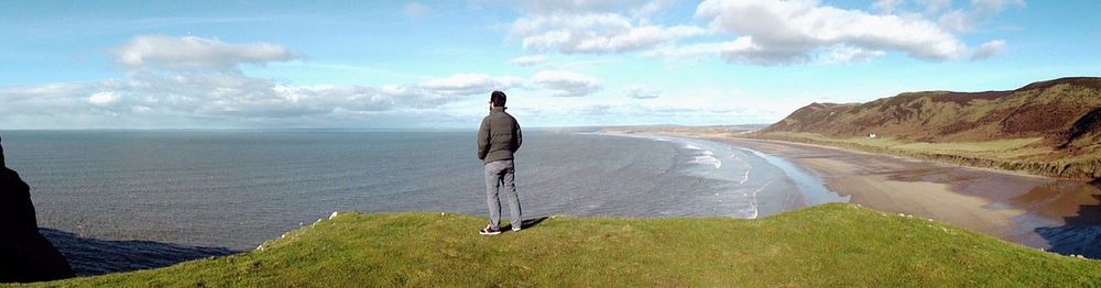 Panoramic view of man standing by sea against cloudy sky