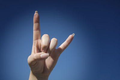 Cropped hand showing horn sign against clear blue sky