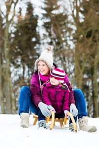 Rear view of girl sitting on snow against trees