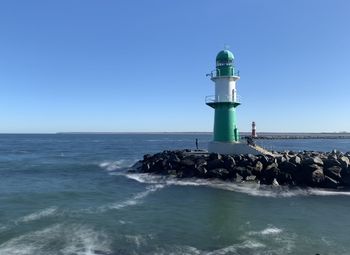 Lighthouse by sea against clear blue sky