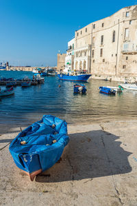 Boats moored in canal by buildings against clear blue sky